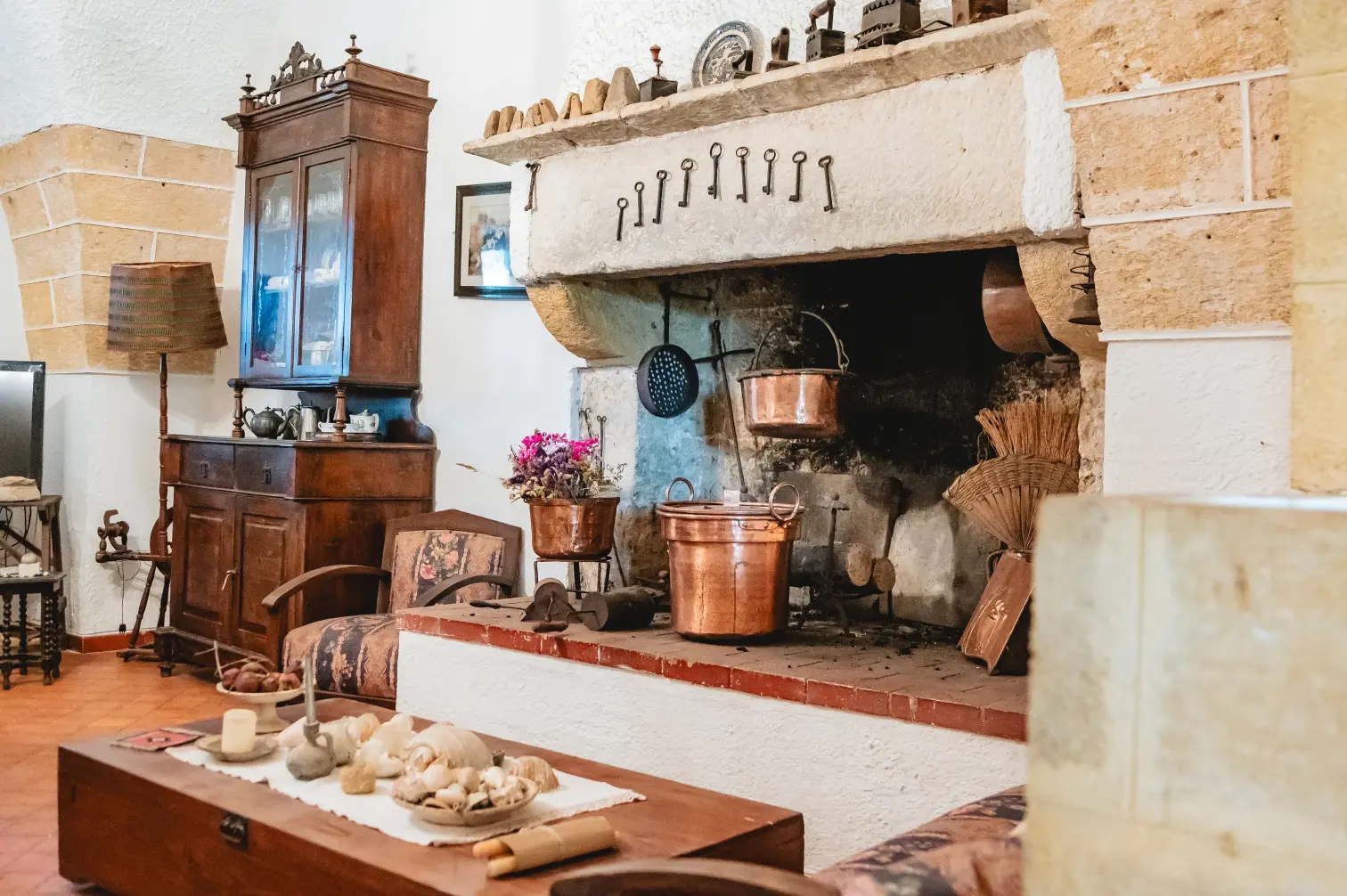 Soggiorno tradizionale con grande camino in pietra decorato con pentole di rame, chiavi antiche e mobili in legno d'epoca