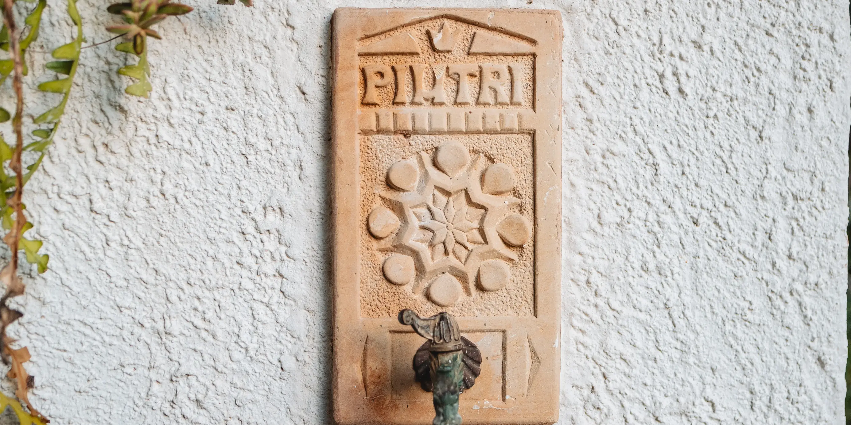 Fontana a muro in terracotta con decorazione floreale scolpita e rubinetto in ottone vintage su parete bianca rugosa