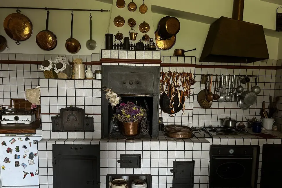 Interno di una cucina rustica con pareti in pietra, mensole in legno fornite di utensili e un tavolo centrale