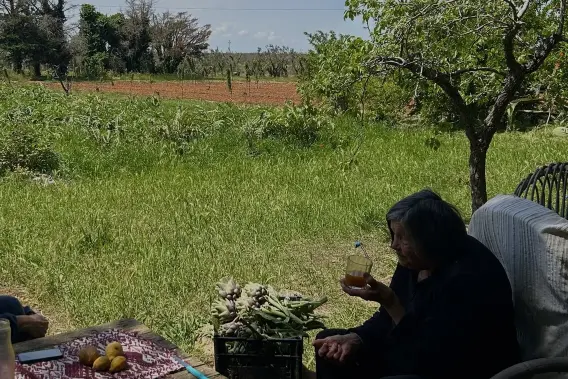 Francesca seduta su una panchina in pietra all'esterno della masseria, circondata dal verde